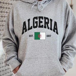 May include: Grey hooded sweatshirt with the text "ALGERIA EST. 1007" and the Algerian flag printed on the front.