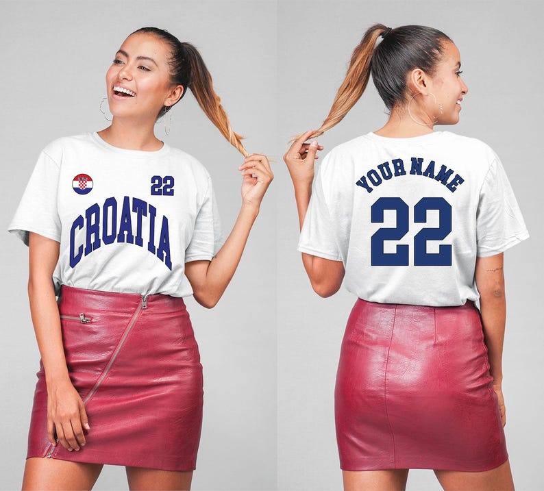 May include: White t-shirt with "CROATIA" in blue lettering, the number 22, and a Croatian flag emblem. The back of the shirt has "YOUR NAME" and the number 22 in blue. The model is wearing a red skirt.