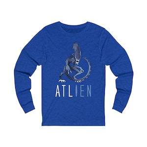 May include: A royal blue long-sleeve t-shirt with a graphic of a blue alien with a tail and the word "ATLIEN" printed in white below the alien.