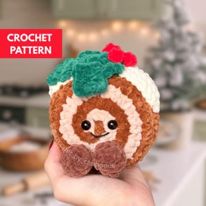 May include: A crocheted Christmas cake roll with a smiling face, brown and white swirls, and green holly with red berries. The text "CROCHET PATTERN" is in a red box. The cake roll has two brown pom-pom feet.