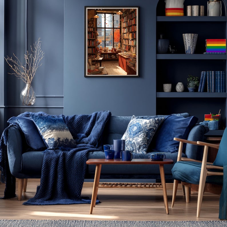 A framed illustration of a bookstore with autumn trees outside, hanging on a blue wall above a blue sofa and wooden coffee table.