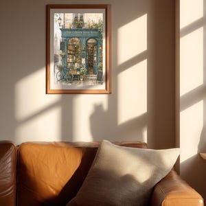 A framed print of "The London Book Nook" hangs on a light-colored wall above a brown leather sofa with a patterned pillow, with sunlight casting shadows.