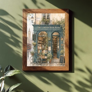 A framed print of a watercolor illustration of a blue-green storefront with "THE LONDON BOOK NOOK" above the door, a bicycle parked outside, and Big Ben in the background, hanging on a dark green wall with plant shadows.
