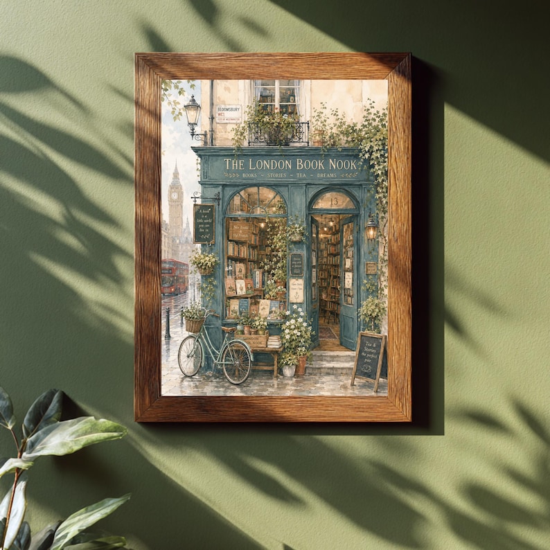 A framed print of a watercolor illustration of a blue-green storefront with "THE LONDON BOOK NOOK" above the door, a bicycle parked outside, and Big Ben in the background, hanging on a dark green wall with plant shadows.