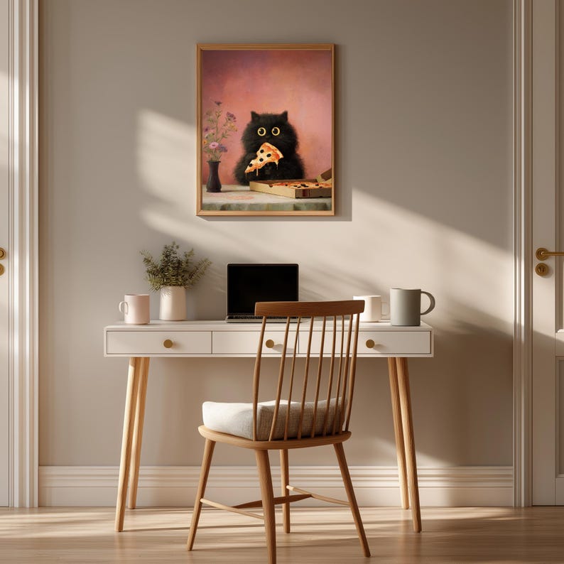 Puede incluir: Una impresi&oacute;n art&iacute;stica enmarcada representa a un gato negro comiendo pizza. El gato tiene grandes ojos amarillos y sostiene una porci&oacute;n de pizza. La obra de arte est&aacute; sobre un fondo rosa. Un escritorio y una silla est&aacute;n en primer plano.