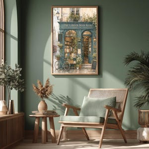 A framed print of a watercolor illustration of a blue-green storefront with "THE LONDON BOOK NOOK" above the door, a bicycle parked outside, and Big Ben in the background, hanging on a dark green wall above a wooden chair and side table.