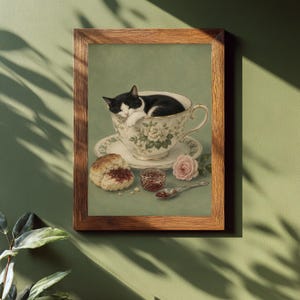 Puede incluir: Una lámina enmarcada que muestra un gato blanco y negro durmiendo dentro de una taza de té floral sobre un platillo. Junto a la taza hay un bollo con mermelada roja, un pequeño tarro de cristal, una cuchara de plata y una rosa de color rosa pálido.