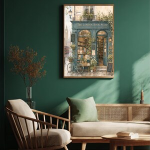 A framed print of a watercolor illustration of a blue-green storefront with "THE LONDON BOOK NOOK" above the door, a bicycle parked outside, and Big Ben in the background, hanging on a dark green wall above a sofa with a green pillow.