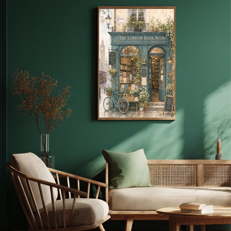 A framed print of a watercolor illustration of a blue-green storefront with "THE LONDON BOOK NOOK" above the door, a bicycle parked outside, and Big Ben in the background, hanging on a dark green wall above a sofa with a green pillow.
