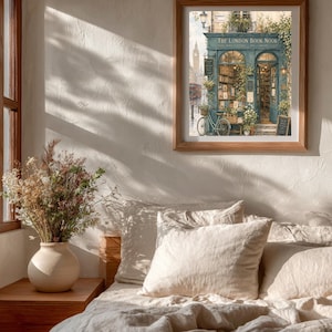 A framed print of "The London Book Nook" hangs on a textured wall above a bed with white linens, with sunlight casting shadows across the room.