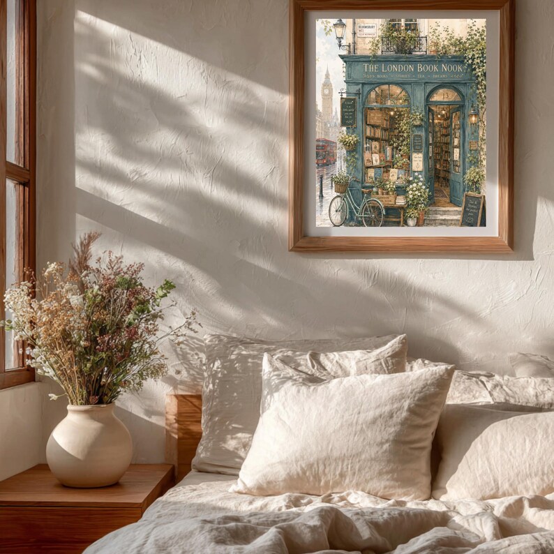 A framed print of "The London Book Nook" hangs on a textured wall above a bed with white linens, with sunlight casting shadows across the room.