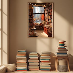 A framed illustration of a bookstore with autumn trees outside, hanging on a light beige wall above stacks of books and a mug.