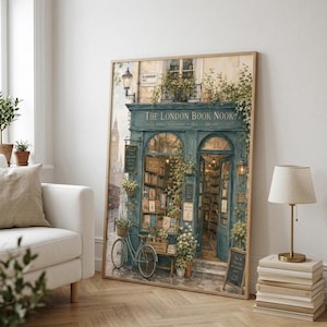A framed print of a watercolor illustration of a blue-green storefront with "THE LONDON BOOK NOOK" above the door, a bicycle parked outside, and Big Ben in the background, leaning against a white sofa in a room with light wood floors.