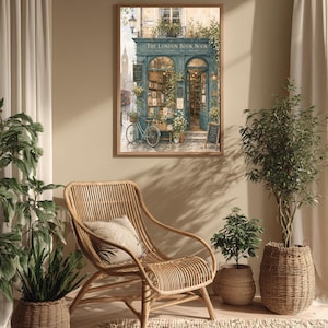 A framed print of a watercolor illustration of a blue-green storefront with "THE LONDON BOOK NOOK" above the door, a bicycle parked outside, and Big Ben in the background, hanging on a light beige wall above a wicker chair.