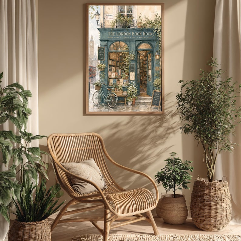 A framed print of a watercolor illustration of a blue-green storefront with "THE LONDON BOOK NOOK" above the door, a bicycle parked outside, and Big Ben in the background, hanging on a light beige wall above a wicker chair.