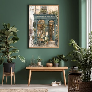 A framed print of a watercolor illustration of a blue-green storefront with "THE LONDON BOOK NOOK" above the door, a bicycle parked outside, and Big Ben in the background, hanging on a dark green wall above a wooden bench with plants.