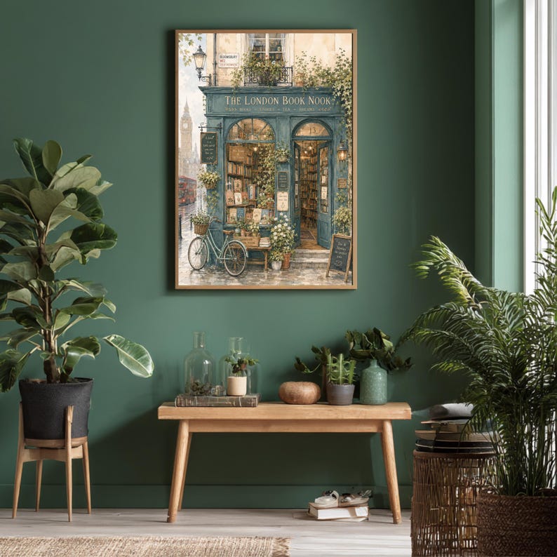 A framed print of a watercolor illustration of a blue-green storefront with "THE LONDON BOOK NOOK" above the door, a bicycle parked outside, and Big Ben in the background, hanging on a dark green wall above a wooden bench with plants.