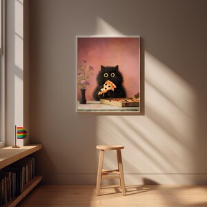 Puede incluir: Impresi&oacute;n enmarcada que muestra un gato negro comiendo una porci&oacute;n de pizza. El gato tiene grandes ojos amarillos y est&aacute; situado frente a un fondo rosa. Tambi&eacute;n se ve una caja de pizza y un jarr&oacute;n con flores.