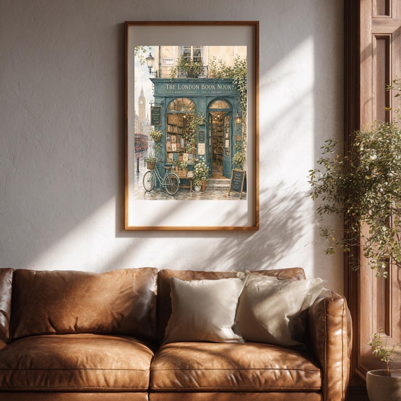 A framed print of "The London Book Nook" hangs on a white wall above a brown leather sofa, with a potted plant to the right.