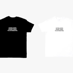 May include: A black short-sleeved t-shirt and a white short-sleeved t-shirt, both featuring the text "HATING AESPA DOESN'T MAKE YOU INTERESTING." printed in a simple, bold, sans-serif font across the center of the chest area on each garment.