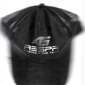 Puede incluir: Gorra de béisbol negra con parte trasera de malla y acabado desgastado. La gorra presenta el texto "45" y "RESPA FORMULA ONE TEAM" en letras plateadas. Tiene una visera curva y un botón en la parte superior.