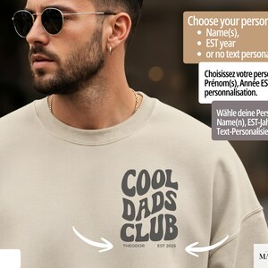 May include: Sand-colored sweatshirt with the text "COOL DADS CLUB" in a retro font. The text includes "THEODOR" and "EST 2025". The sweatshirt offers personalization options for names and EST year.