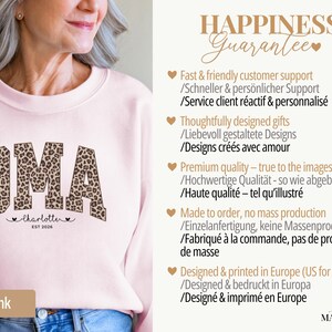 May include: Light pink sweatshirt with the word "OMA" in a leopard print design. Below the word "OMA" is the name "Charlotte" and the year "EST 2026". The sweatshirt is part of a gift collection.