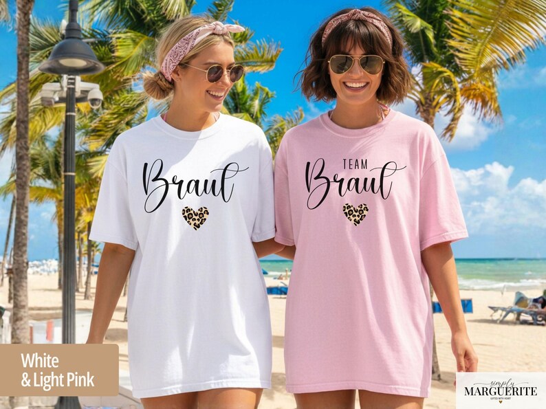 Pu&ograve; includere: Due donne indossano magliette bianche e rosa chiaro. La maglietta bianca dice "Braut" e quella rosa "Team Braut". Entrambe hanno un carattere script e un design a cuore leopardato.