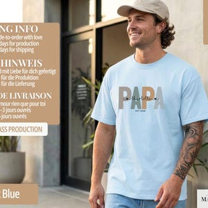 Puede incluir: Camiseta azul claro con la palabra "PAPA" en un dise&ntilde;o multicolor, el nombre "Charlotte" y el a&ntilde;o "EST 2020". La camiseta est&aacute; hecha de un material suave.