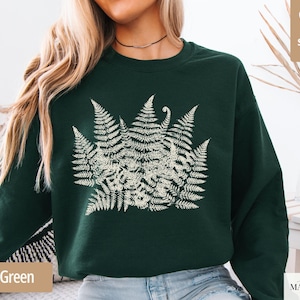 Puede incluir: Sudadera verde bosque con un dise&ntilde;o de helecho crema. La ilustraci&oacute;n bot&aacute;nica est&aacute; centrada en el pecho. La sudadera tiene cuello redondo y mangas largas. Las palabras "super soft" est&aacute;n en un coraz&oacute;n en la esquina superior derecha.