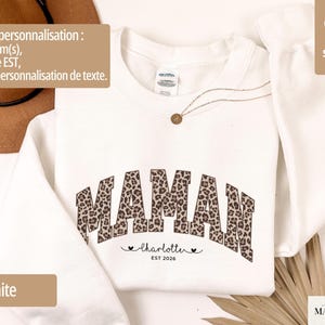 Op de afbeelding: Witte sweatshirt met het woord "MAMAN" in een luipaardprint. Daaronder de naam "Charlotte" en het jaar "EST 2026". De sweatshirt heeft een "super soft" label.