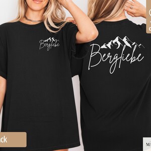 May include: Black t-shirt with the word "Bergliebe" and a mountain range graphic in white on the front and back. The shirt is made of 100% cotton.