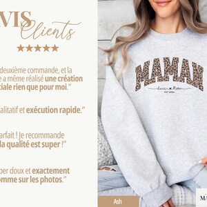 Op de afbeelding: Een lichtgrijs sweatshirt met het woord "MAMAN" in een luipaardprint ontwerp over de borst. Onder het woord "MAMAN" staat de tekst "Laca Rose EST 2024". De sweatshirt heeft een casual stijl.
