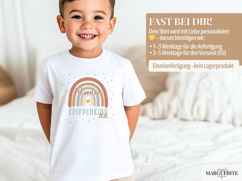 May include: A white short-sleeved t-shirt featuring a graphic of a multi-colored rainbow in shades of brown, blue, and cream. The design includes the name Theodor, the text KRIPPENKIND, the year 2026, a small yellow heart, and scattered gold dots.