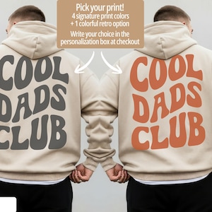 May include: Two beige hoodies with the text "COOL DADS CLUB" in gray and orange. The image includes text that says "Pick your print! 4 signature print colors + 1 colorful retro option. Write your choice in the personalization box at checkout."