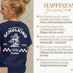 May include: A navy blue t-shirt featuring a white graphic on the back. The design includes the text SCHULKIND, PROUD MEMBER OF THE CLUB, EST 2026, EINFACH 1. KLASSE, and the name Sophie, alongside a cartoon character wearing sunglasses.