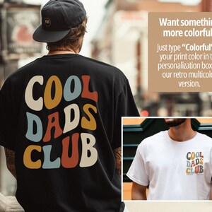 May include: Black t-shirt with the words "COOL DADS CLUB" in a retro font on the back. The text is in various colors, including yellow, blue, orange, and white. A smaller image shows a white t-shirt with the same design.