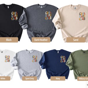 May include: A selection of crewneck sweatshirts in various colors, including black, dark heather, sand, white, sport grey, navy, and military green. Each sweatshirt features the text "COOL DADS CLUB" in a retro font on the chest.