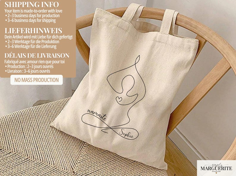 May include: Beige canvas tote bag with black line art of a yoga pose, a heart, and the words "namaste Sophie." The bag has two handles and is sitting on a woven chair. The bag is made of a natural material.