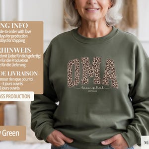 May include: An olive green sweatshirt with the word "OMA" in a leopard print design. Below the word "OMA" is the text "Emma & Noah" and the year "EST 2026". The sweatshirt is a crew neck style.