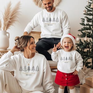 Pode incluir: Camisolas brancas a condizer com gola redonda, apresentando um gráfico de linhas pretas de cinco árvores de Natal estilizadas sobre o texto dourado Merry Christmas e Family Martin. As peças têm mangas compridas e gola, punhos e bainha canelados.