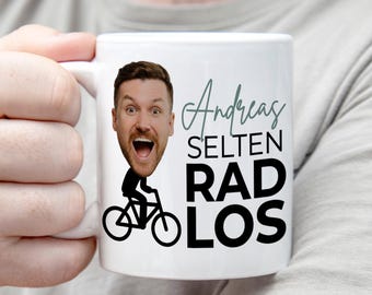 May include: A white ceramic mug featuring a graphic of a person riding a bicycle with a large photographic head cutout. The text reads Andreas SELTEN RAD LOS in a mix of script and bold sans-serif fonts, with the head showing a wide-mouthed expression.