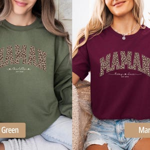 Op de afbeelding: Olijfgroene sweatshirt en bordeauxrode t-shirt, beide met het woord "MAMAH" in een luipaardprint. De sweatshirt heeft "Charlotte" en de t-shirt "Romy & Luca" eronder, met het jaar "EST 2024".