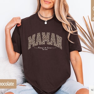 Op de afbeelding: Donker chocoladebruin t-shirt met het woord "MAMAR" in een luipaardprint. Onder het woord "MAMAR" staat de tekst "Romy & Luca" en het jaar "EST 2024". Het shirt is gemaakt van 100% katoen.