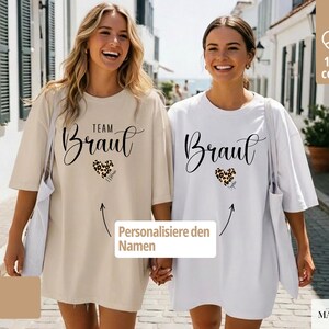 Pu&ograve; includere: Due donne indossano magliette oversize. Una &egrave; color sabbia, l'altra bianca. Entrambe le magliette hanno la parola "Braut" in corsivo, un cuore leopardato e la scritta "Team Braut" su una. Le magliette sono in 100% cotone.