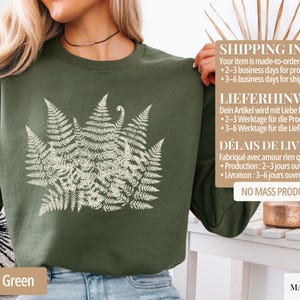 Puede incluir: Sudadera verde militar con un dise&ntilde;o de helecho blanco. La parte superior de manga larga tiene cuello redondo. El texto "Military Green" est&aacute; en la parte inferior de la imagen. La sudadera es de material suave.