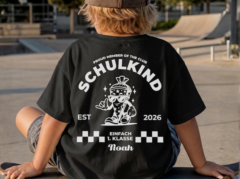 May include: A black t-shirt featuring a white graphic on the back. The design includes the text "PROUD MEMBER OF THE CLUB SCHULKIND", "EST 2026", and "EINFACH 1. KLASSE" with the name "Noah". A cartoon character wearing sunglasses is centered.