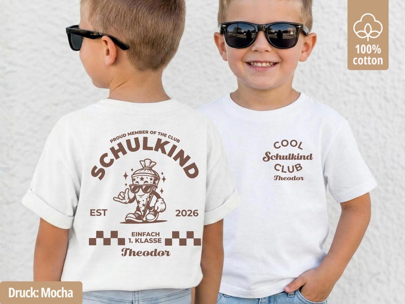 May include: A white t-shirt featuring brown graphic prints. The back displays a cartoon school cone character with sunglasses, the text SCHULKIND, EST 2026, EINFACH 1. KLASSE, and the name Theodor. The front shows the text COOL Schulkind CLUB Theodor.