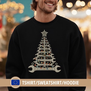Puede incluir: Sudadera negra con un diseño de árbol de Navidad hecho con llaves inglesas, una estrella y luces de cadena. El texto "TSHIRT/SWEATSHIRT/HOODIE" está en la parte inferior. El diseño utiliza tonos grises, beige y marrones.