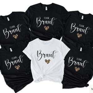 Pu&ograve; includere: Una collezione di magliette nere e bianche. Ogni maglietta presenta la scritta "Team Braut" in un carattere corsivo, con un cuore con stampa leopardata. Le magliette sono probabilmente per un addio al nubilato.